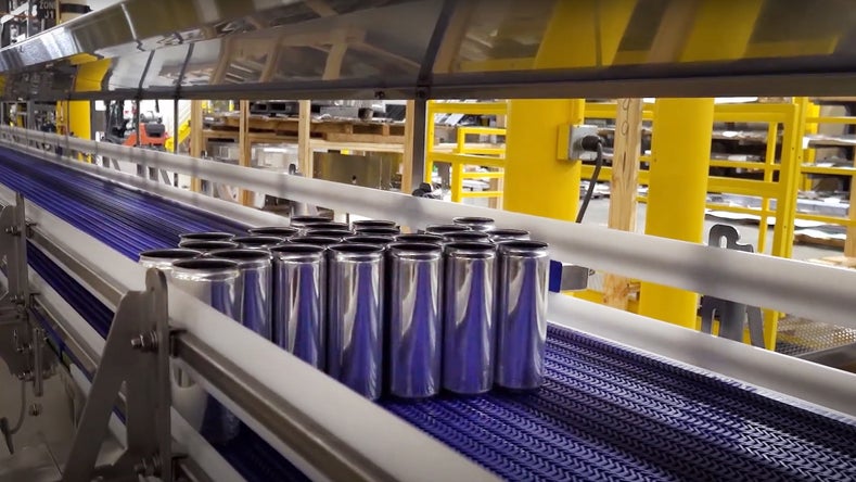 Industrial conveyor belt system transporting aluminum beverage cans through automated production line in modern manufacturing facility.