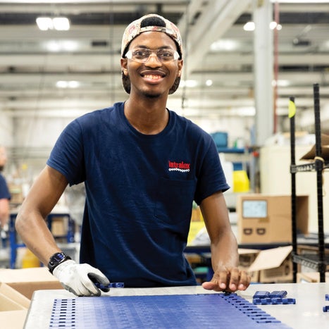 Intralox employee wearing backwards baseball cap and safety glasses assembling blue conveyor belt