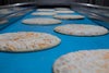 Unbaked pizzas on ThermoDrive flat top conveyor belt