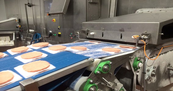 Raw burger patties on tissue paper entering freezer spiral conveyor