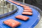 Shrink-wrapped tray packs of ground meat curving around a radius conveyor with S2400 Heavy Duty Edge belting