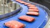Shrink-wrapped tray packs of ground meat curving around a radius conveyor with S2400 Heavy Duty Edge belting