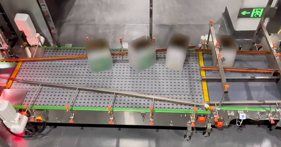 System taśm przenośnikowych z przemieszczającymi się opakowaniami, otoczony różnymi elementami mechanicznymi i barierami bezpieczeństwa.