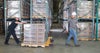 Two workers use a pallet truck to move boxes in a warehouse