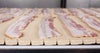Uncooked bacon strips on Series 900 Raised Rib Heavy Duty Edge conveyor belt