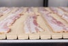 Uncooked bacon strips on Series 900 Raised Rib Heavy Duty Edge conveyor belt