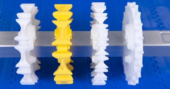 Four CleanLock sprockets of differing size, shape, and color mounted on a CleanLock shaft with blue conveyor belt in background