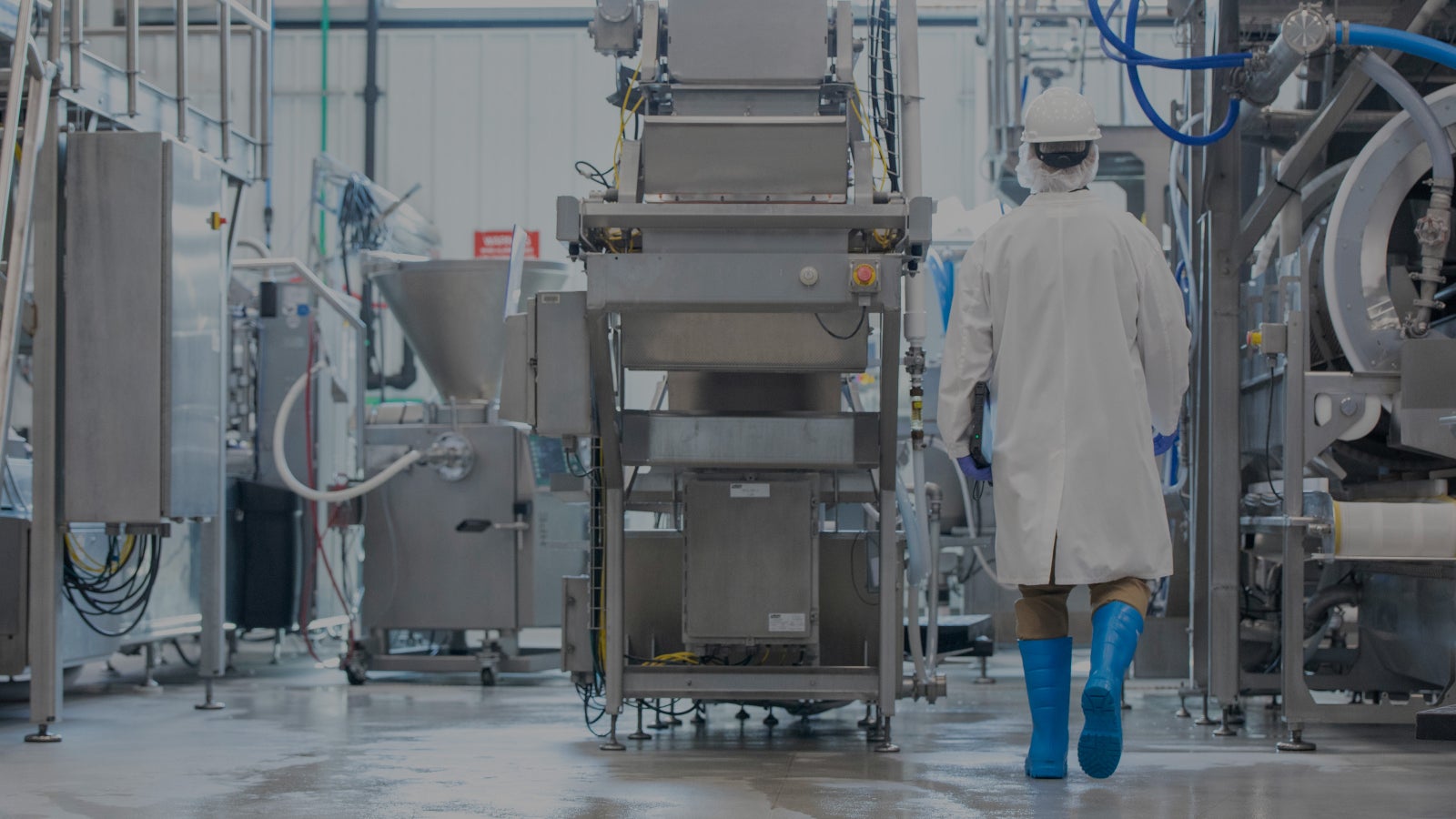 Backside of person in white protective gear walking toward manufacturing equipment, darkened 35%