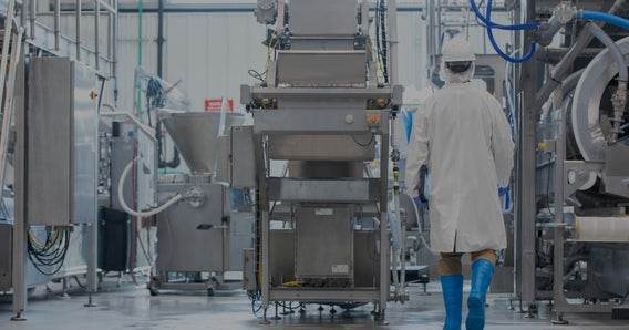 Backside of person in white protective gear walking toward manufacturing equipment, darkened 35%