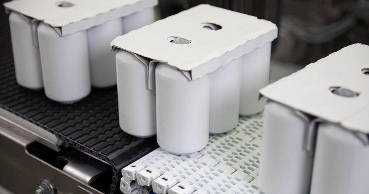 Seis latas de alumínio brancas com suportes de papelão sendo transportadas em uma transferência