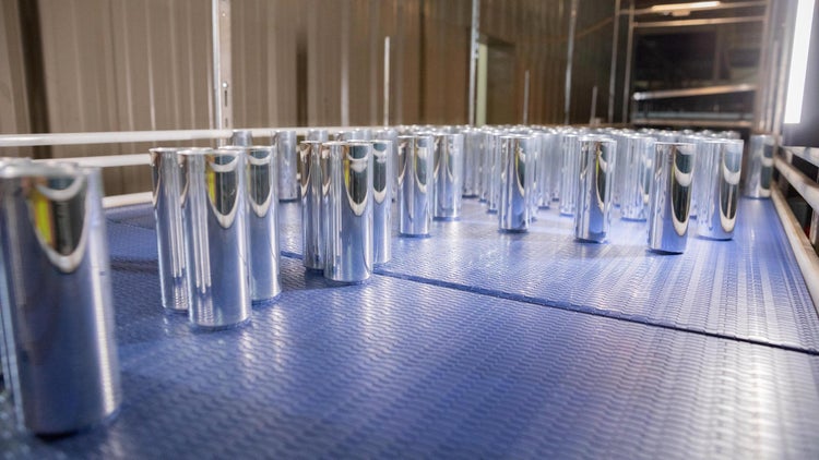 Rangée de cannettes métalliques argentées disposées sur un tapis transporteur bleu