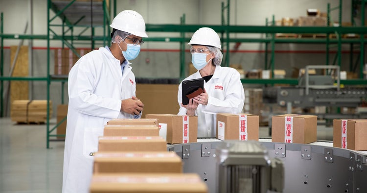 Mitarbeiter in Masken und weißen Kitteln an einer Verpackungslinie