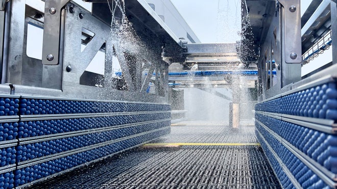 Automatisiertes Clean-in-Place-Modul (CIP) von Intralox sprüht Wasser auf ein leeres Förderband für Getränke