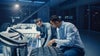Dois trabalhadores de escritório, do sexo masculino, examinando pneus e equipamentos automotivos