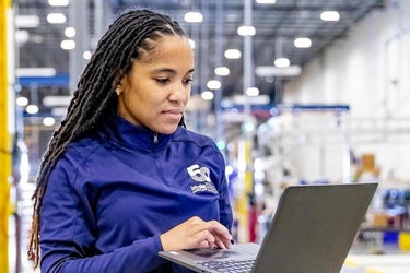 Montadora segurando um laptop dentro de um depósito