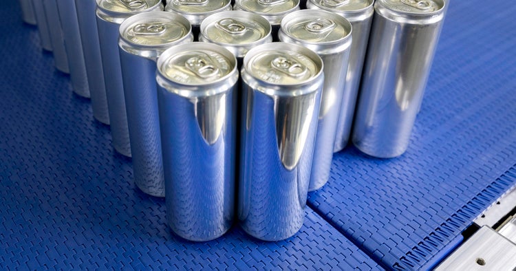 A group of filled aluminum beverage cans sits on a blue conveyor belt in a production facility.