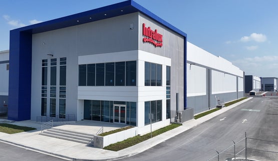 Front exterior of the new Intralox facility in Mexico, showing a modern two-story glass entryway with the Intralox logo and adjacent industrial warehouse space.