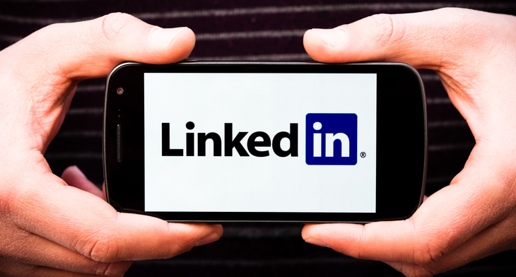 Man's hands holding a cell phone with the LinkedIn logo on the screen.