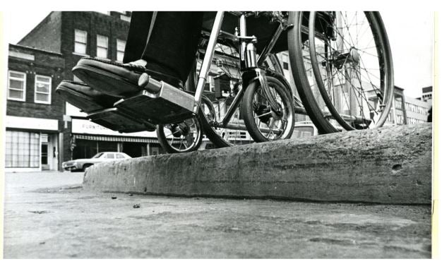 Close-up of wheelchair wheels perched at the edge of an city curb.