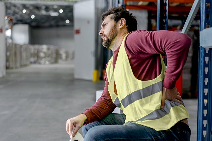 Man sitting in warehouse dealing with back pain.