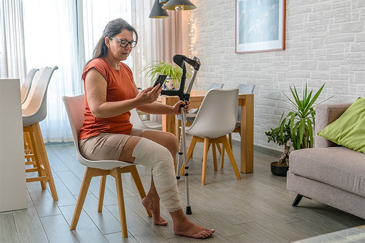 Seated woman with crutches look at her phone