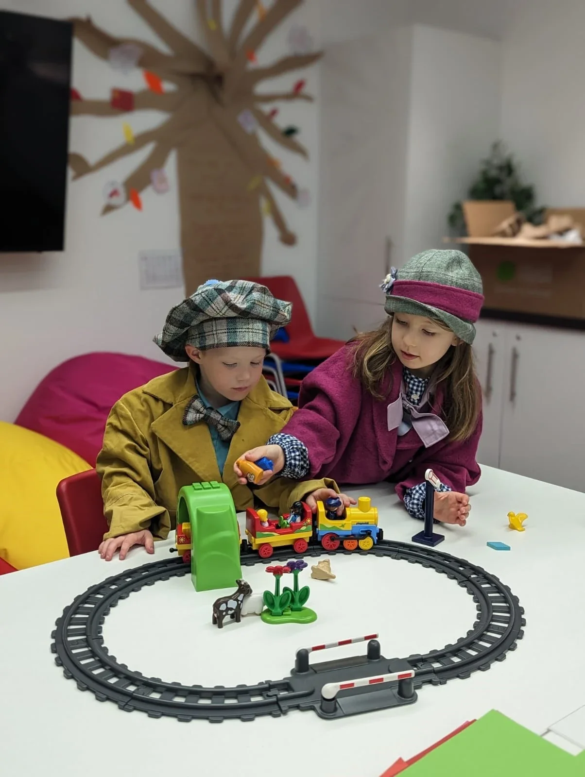 Two children in 1920s fancy dress play with a toy train set.