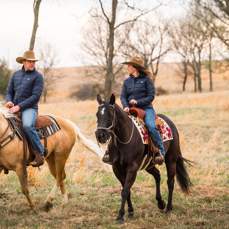 Two horse riders in cowboy hats riding on their horses in an open field