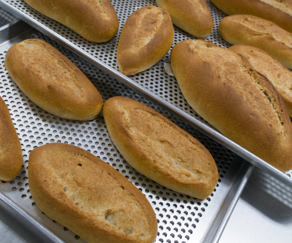 Silver bread tray with perforated base holding several baked rolls