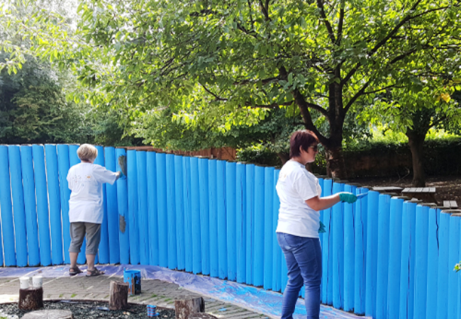 two people painting fence blue in Stowmarket, UK 