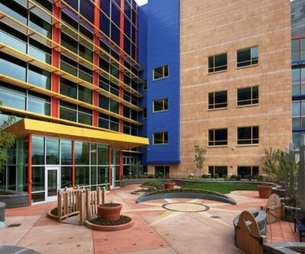 Colorful children's hospital building painted in red, yellow and blue with an inviting outdoor entrance with play area and plants