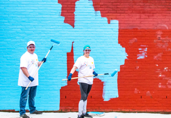 two volunteers painting a red wall blue