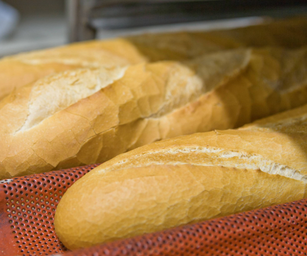 Red bread tray with perforated base holding several baked baguettes