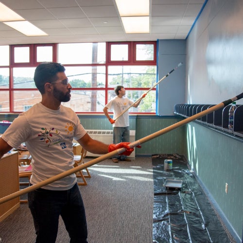 Two volunteers painting a classroom wall with roller brushes 