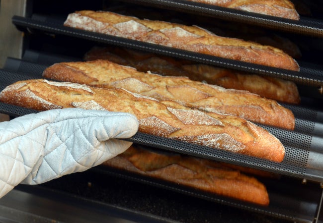 Close-up view of freshly baked baguettes being removed from an oven with a gloved hand