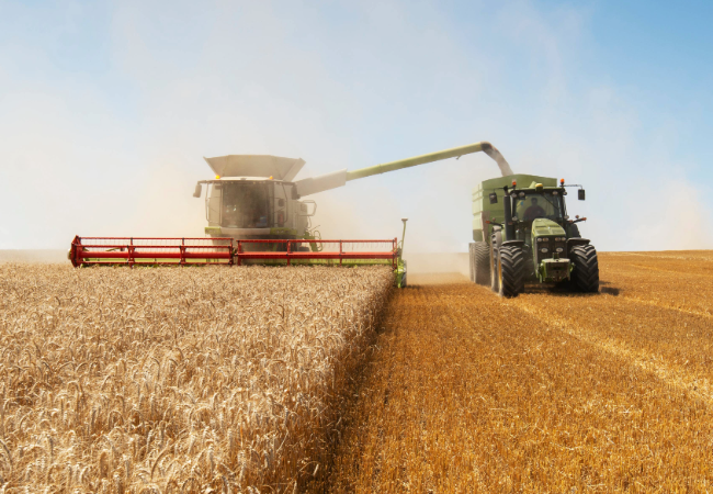 Green tractor protected by PPG's coatings for heavy-duty agricultural equipment, in a field with a cloudy blue sky.