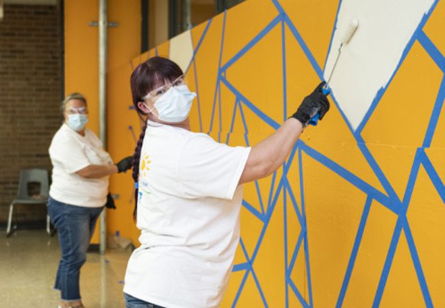 women painting yellow mural