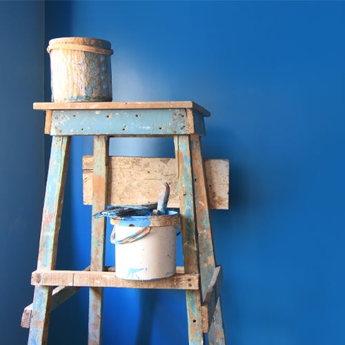Paint bucket and latter in front of blue wall 