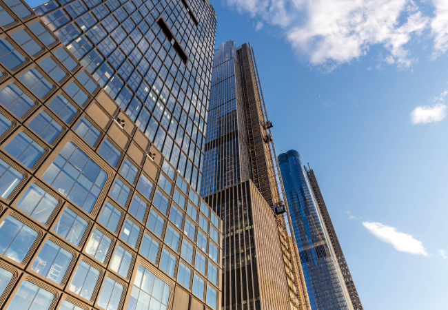 Low angle view of modern glass skyscrapers against a clear blue sky with fluffy clouds.