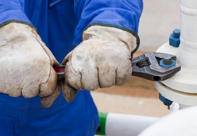 Close-up of a worker's hands using a wrench to tighten a fastener on a white metal pipe protected by PPG fastener coatings.