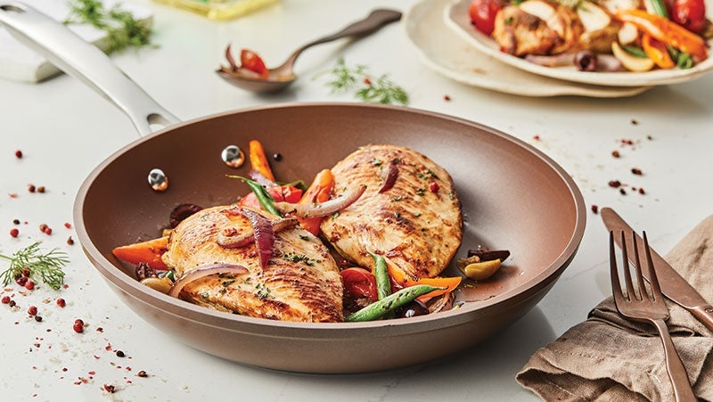 Grilled chicken breast with seasoned vegetables in a modern non-stick frying pan, presented on a neatly set dining table