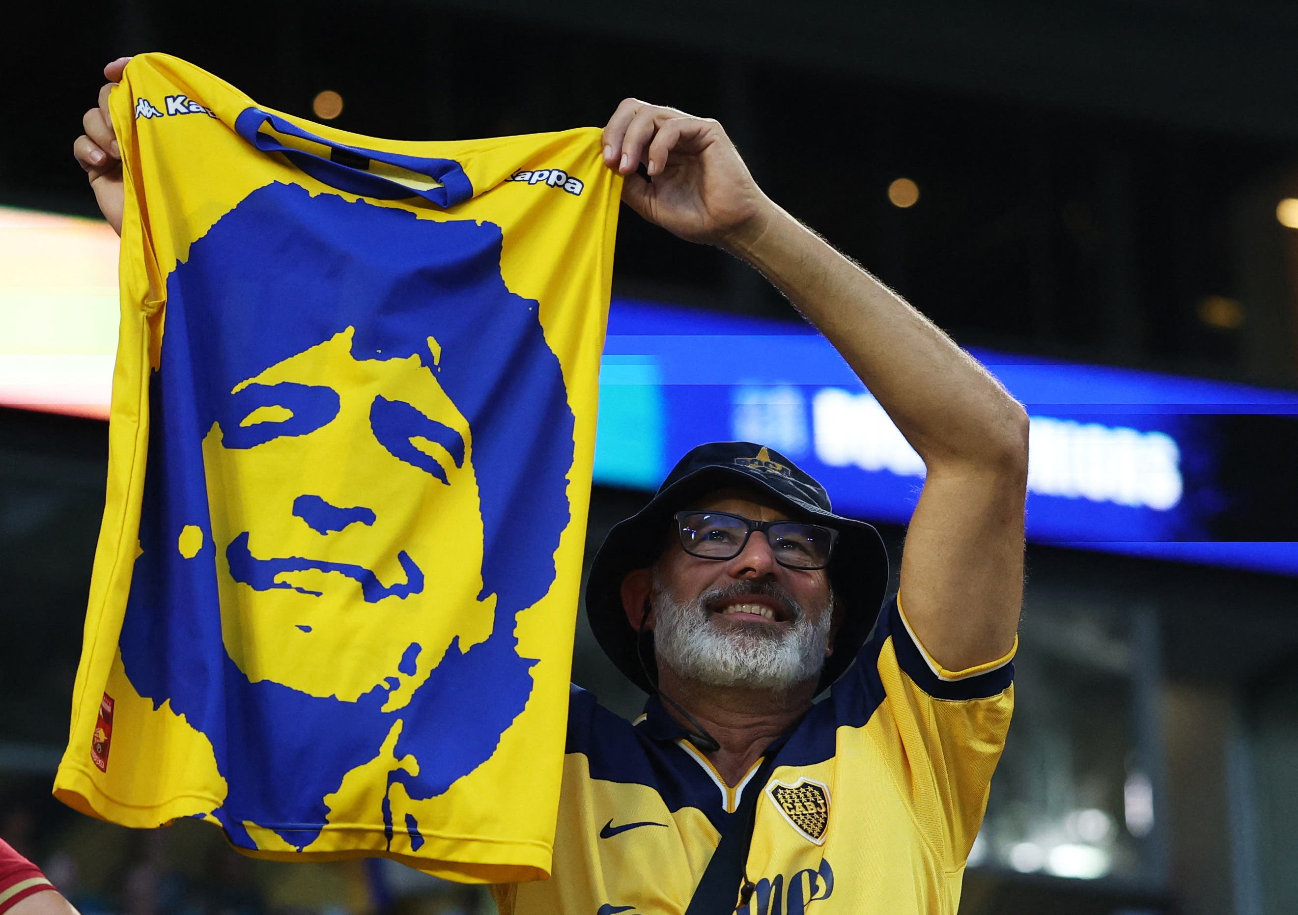 A Boca Juniors fan holds up a shirt displaying the image of former player Diego Maradona in the stands before the match 