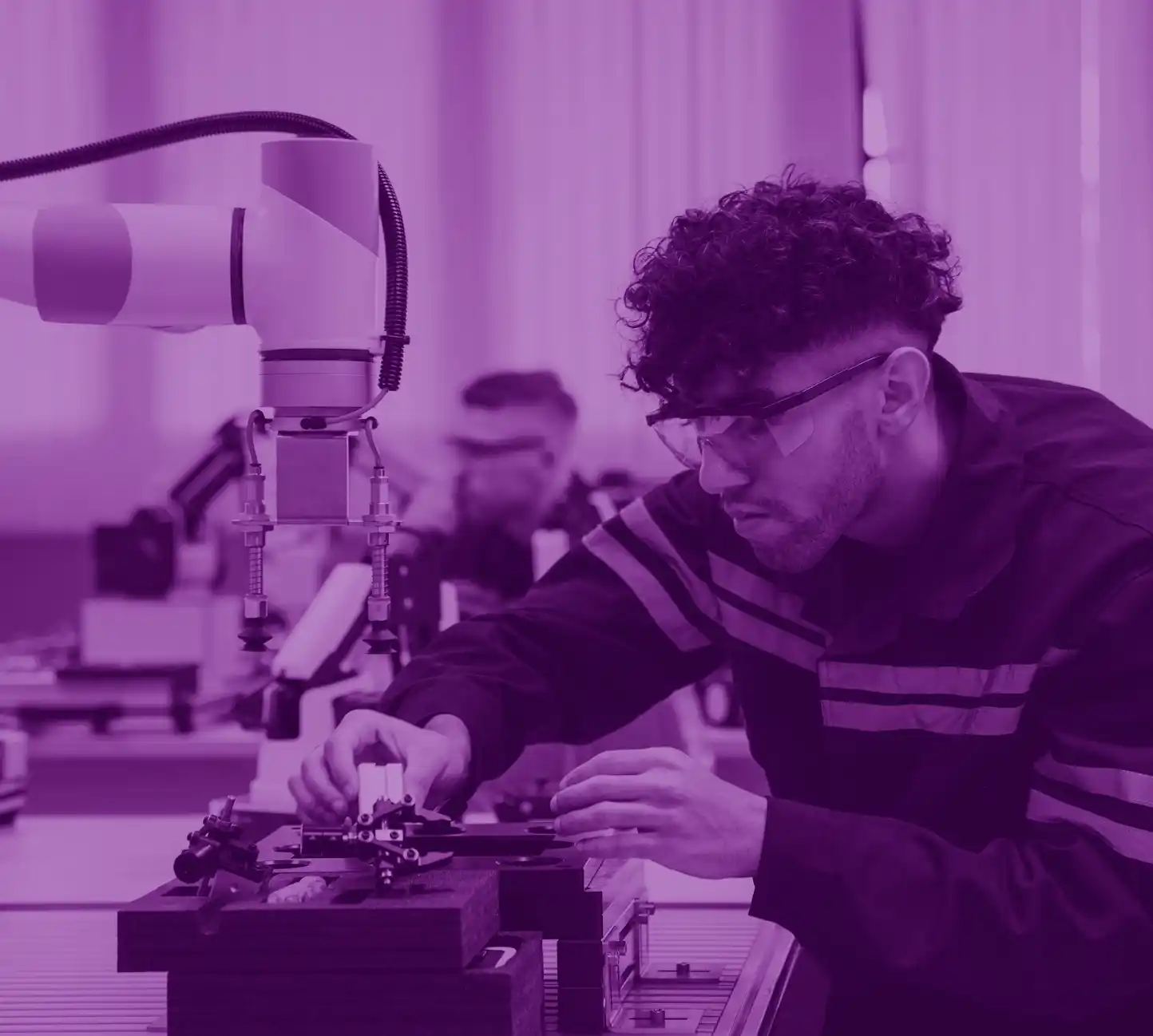 Student wearing safety goggles monitoring a robot in an engineering lab