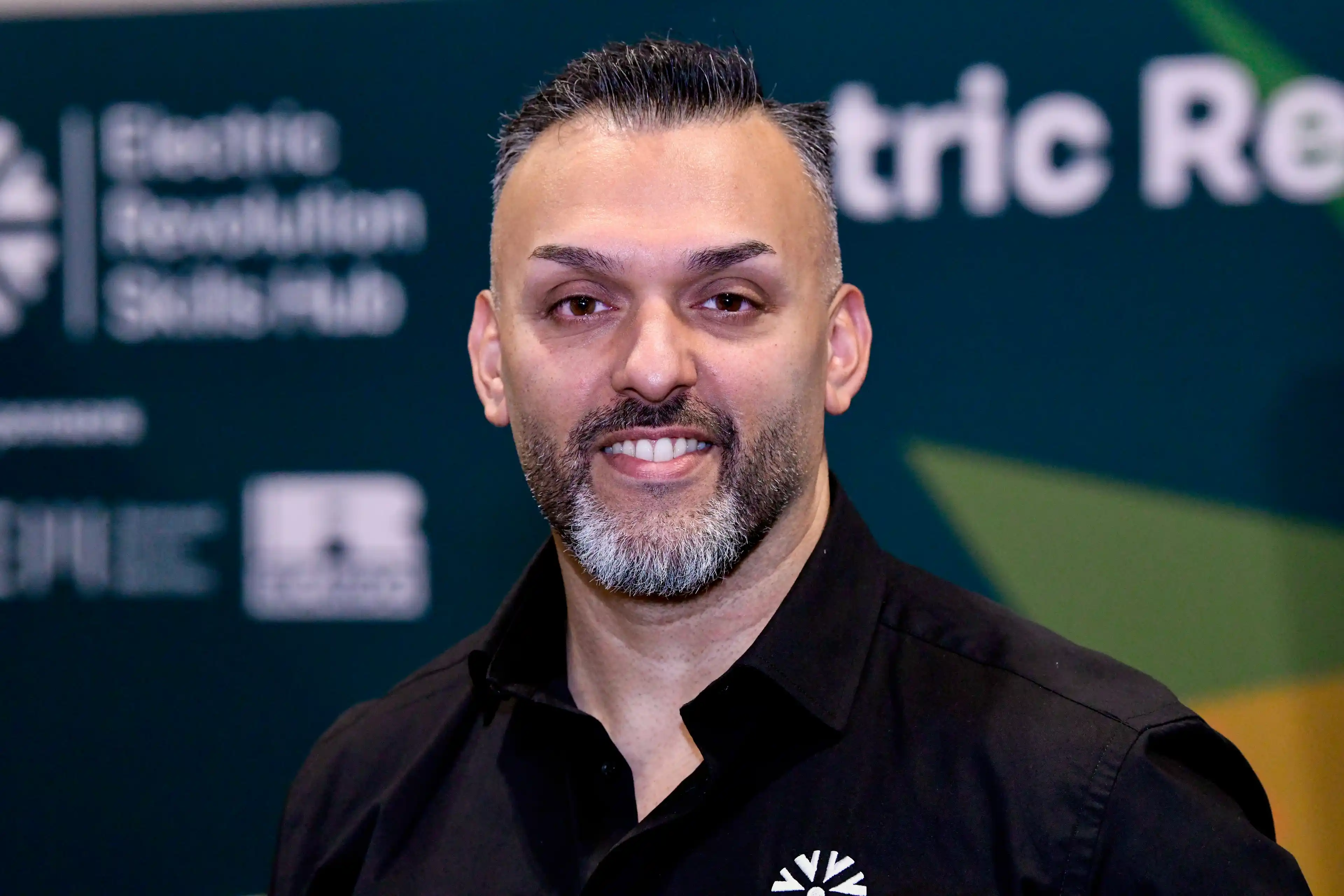 Deepak Farmah smiling at the camera in front of a branded background