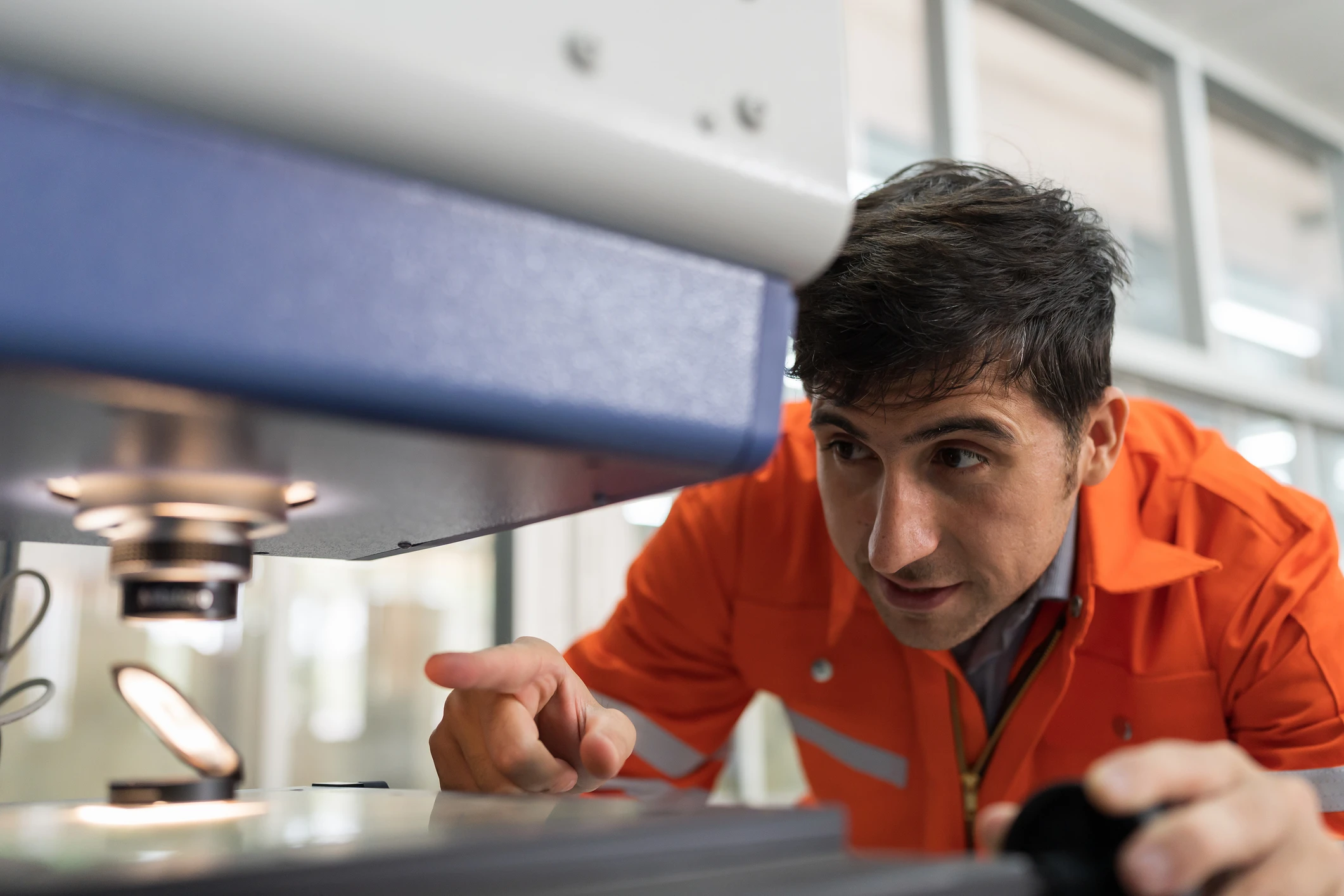 A person in an orange jacket looking at a machine.