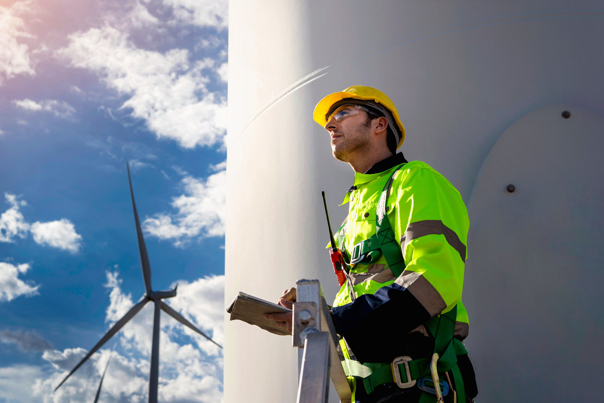 Engineer in hard hat and high vis jacket standing next to wind turbines