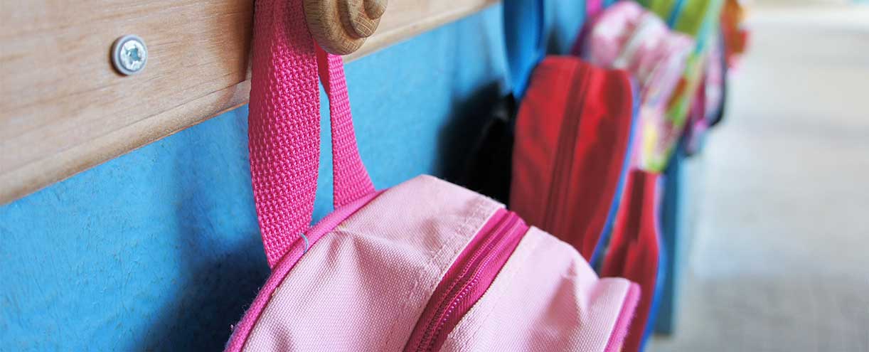 A photo of an elementary school classroom where backpacks are hanging on wall hooks.