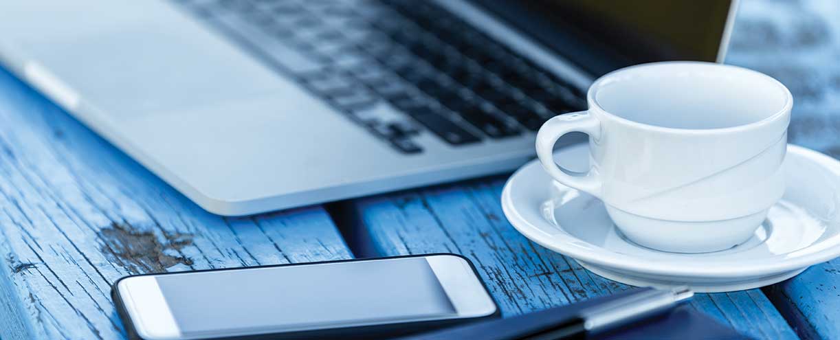 A phone, a cup with saucer, and a laptop on a desk