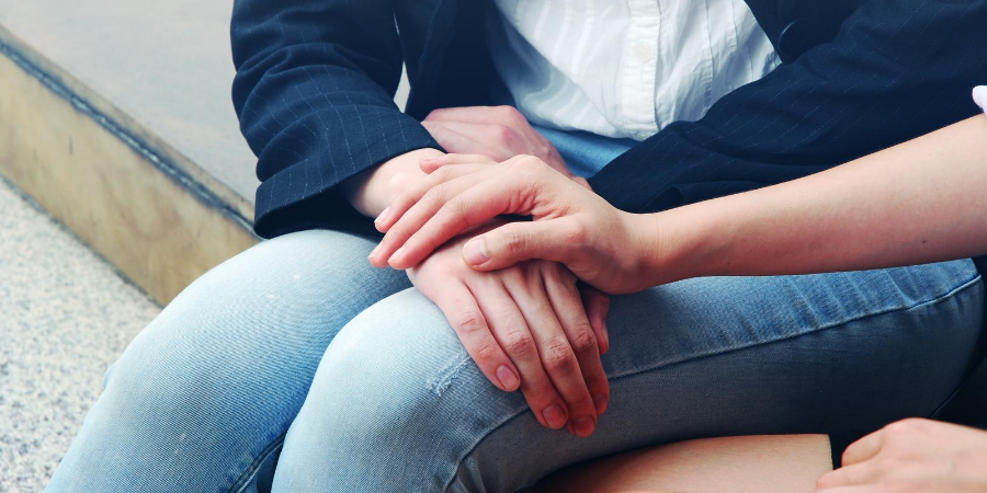 Image of sitting person holding hands with another person who appears to be comforting them