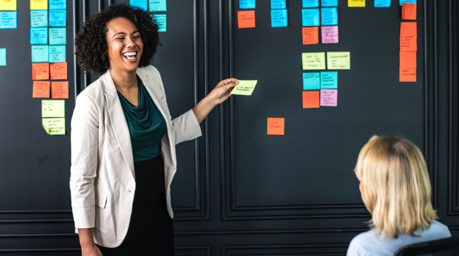 photo of black woman laughing and putting sticky notes on a black wall