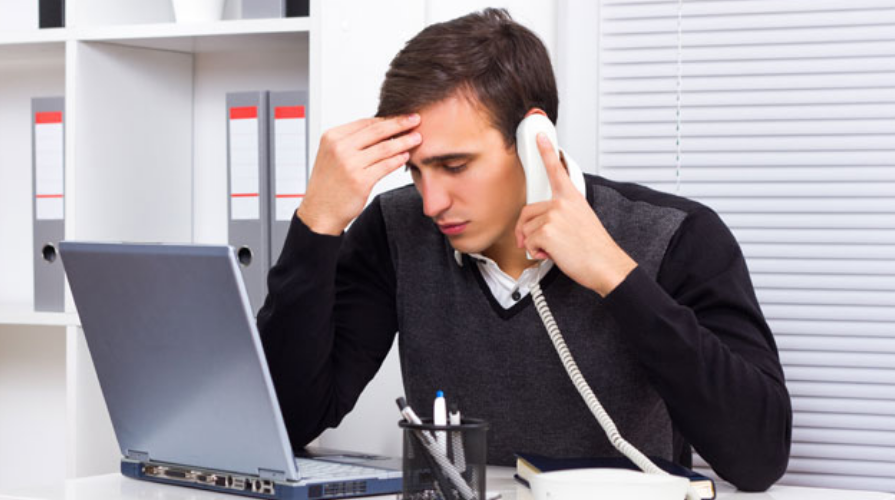 photo of a frustrated man on the phone in front of a laptop computer